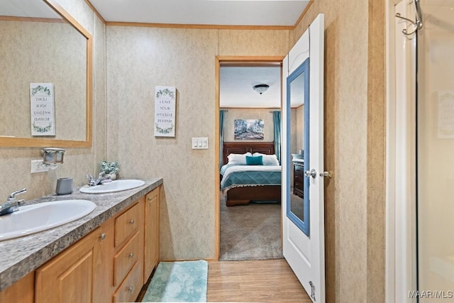 full bathroom featuring wallpapered walls, wood finished floors, a sink, and ensuite bathroom