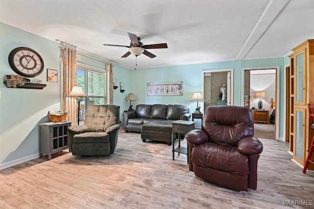 living area featuring a ceiling fan, a textured ceiling, baseboards, and wood finished floors