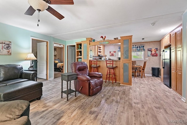 living area featuring ceiling fan, light wood finished floors, and baseboards