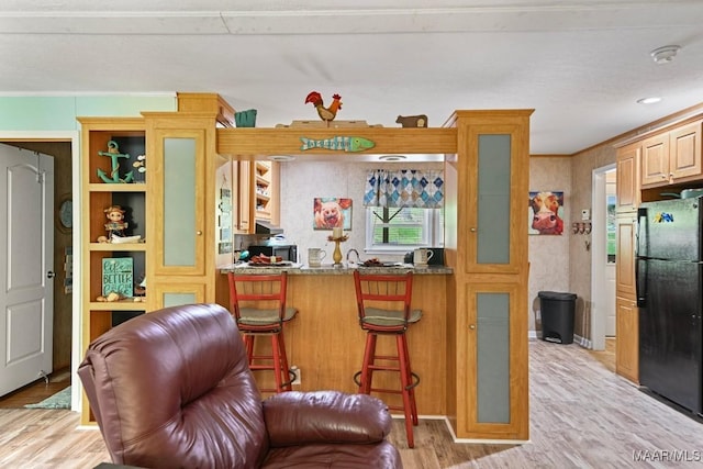 kitchen featuring light wood-type flooring, stone counters, a breakfast bar, and freestanding refrigerator