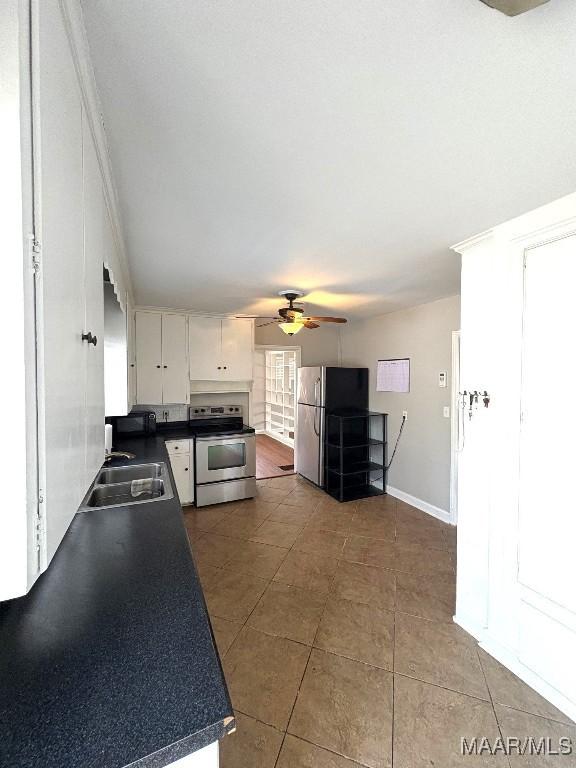 kitchen with dark countertops, appliances with stainless steel finishes, white cabinets, a sink, and tile patterned flooring