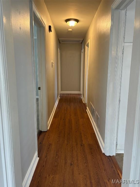 hall with dark wood-style floors, baseboards, and visible vents