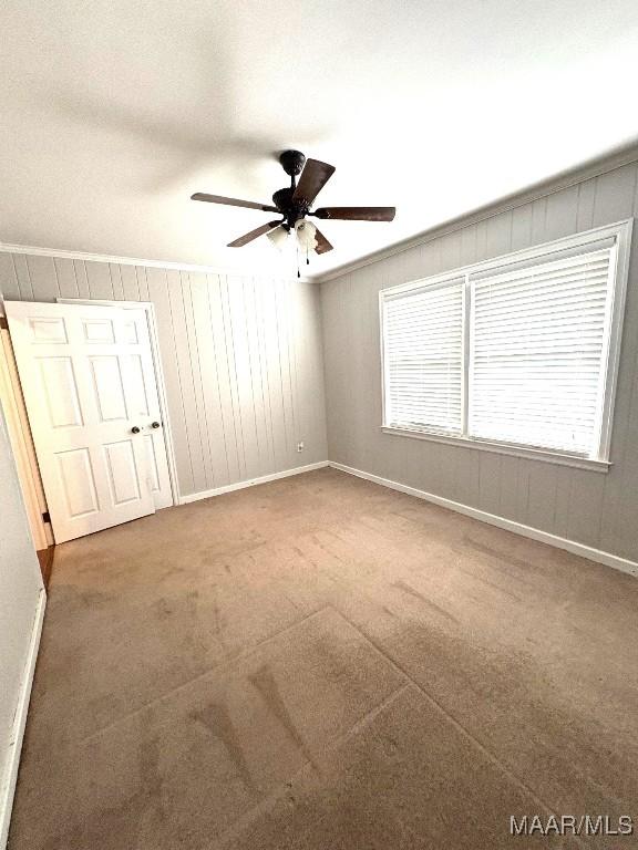 spare room with crown molding, dark carpet, a ceiling fan, and baseboards