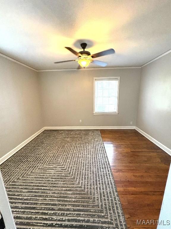 empty room featuring ornamental molding, dark wood finished floors, baseboards, and a ceiling fan