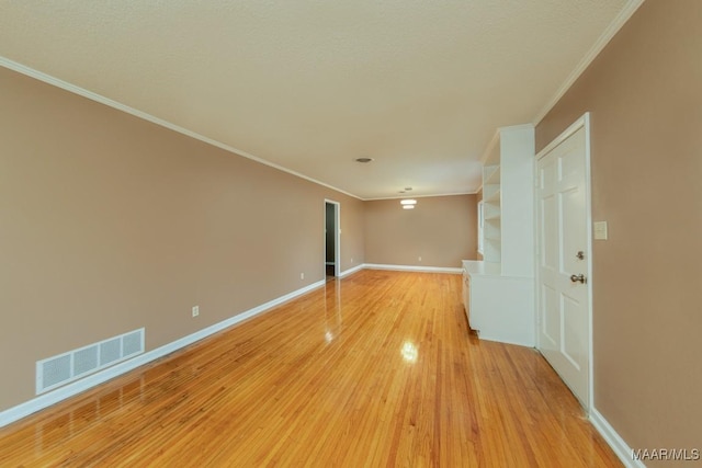 spare room with ornamental molding, light wood-type flooring, visible vents, and baseboards