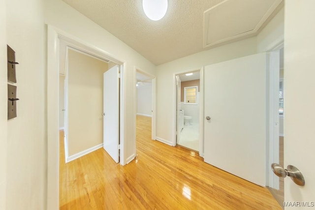 hall featuring attic access, a textured ceiling, baseboards, and wood finished floors