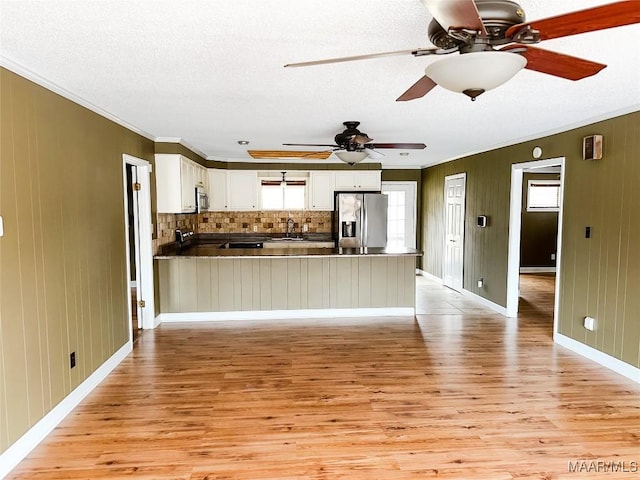 kitchen with stainless steel appliances, a peninsula, white cabinets, light wood-type flooring, and dark countertops