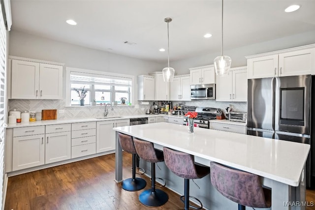 kitchen featuring stainless steel appliances, light countertops, hanging light fixtures, and white cabinetry