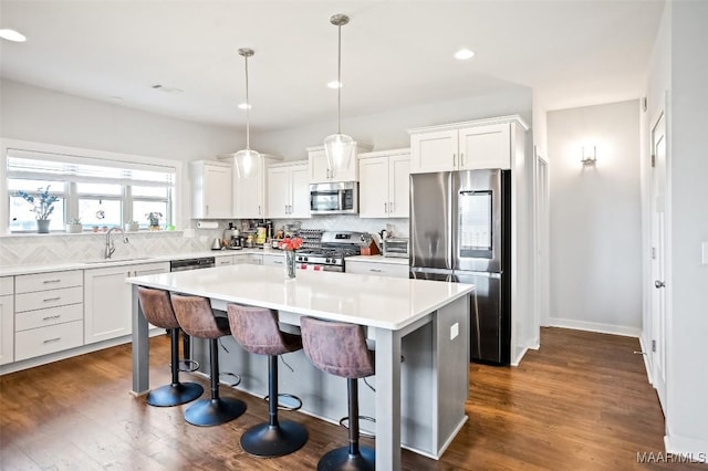 kitchen with decorative light fixtures, light countertops, appliances with stainless steel finishes, white cabinets, and a kitchen island