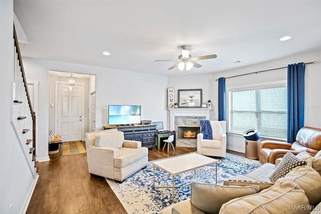 living room featuring ceiling fan, a fireplace, baseboards, stairs, and dark wood-style floors