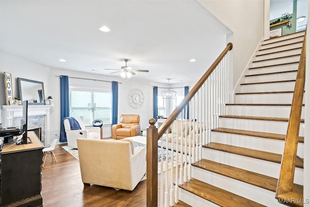 stairs featuring baseboards, a high end fireplace, wood finished floors, ceiling fan with notable chandelier, and recessed lighting