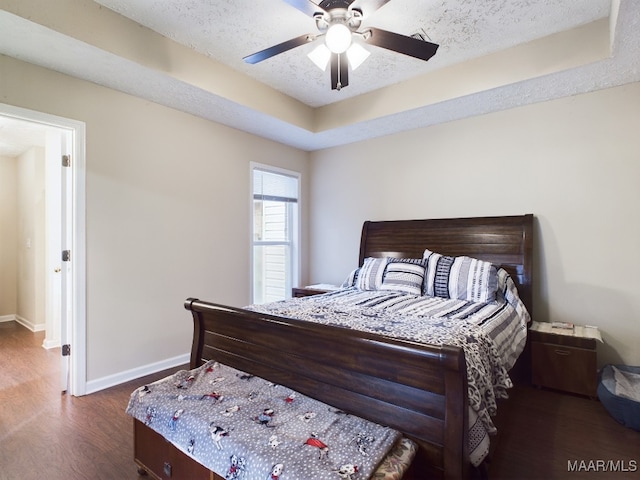 bedroom with baseboards, a ceiling fan, dark wood-type flooring, a tray ceiling, and a textured ceiling