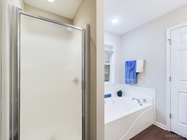 full bath featuring a textured ceiling, wood finished floors, a shower stall, and a bath