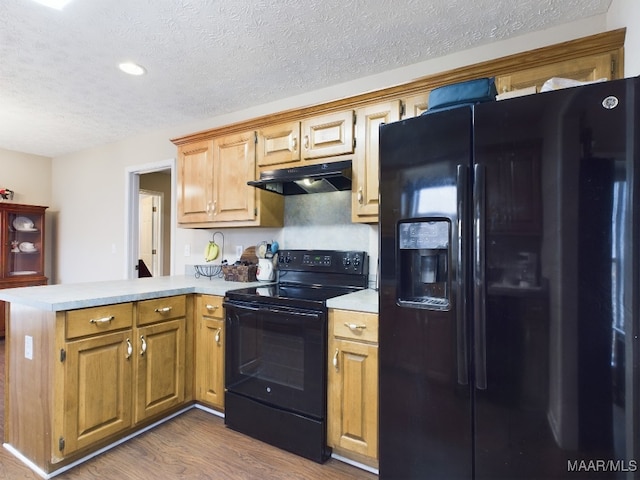 kitchen with a textured ceiling, under cabinet range hood, a peninsula, light countertops, and black appliances