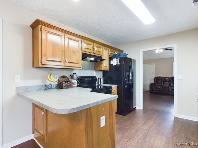 kitchen featuring light countertops, black appliances, dark wood-style flooring, and under cabinet range hood