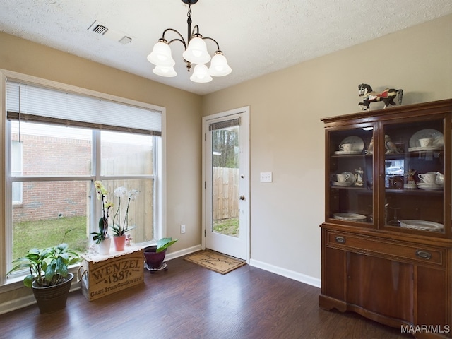 entryway featuring a notable chandelier, dark wood finished floors, visible vents, a textured ceiling, and baseboards