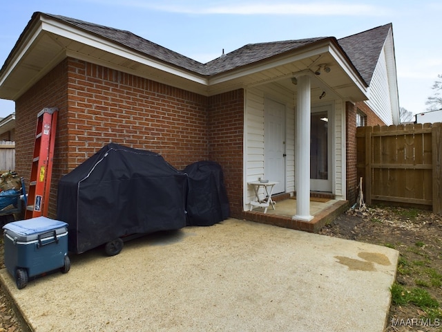 view of side of property featuring roof with shingles, brick siding, fence, and a patio