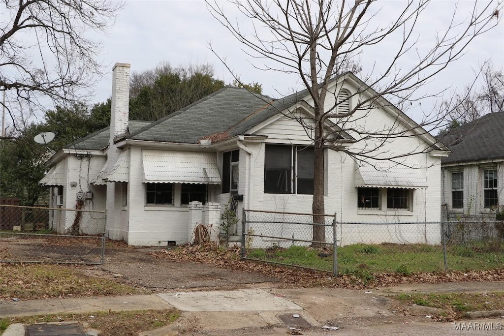 bungalow with roof with shingles, brick siding, a fenced front yard, and a chimney