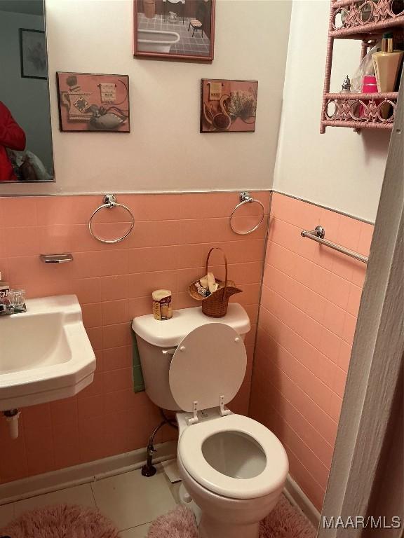 half bath with wainscoting, tile walls, toilet, and tile patterned floors