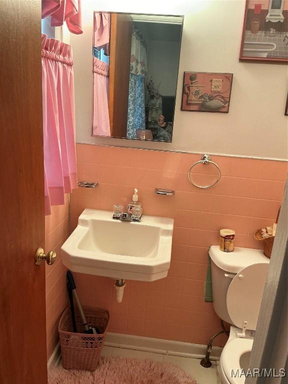 bathroom with wainscoting, a sink, tile walls, and toilet