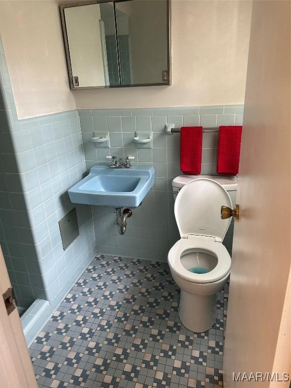 bathroom with wainscoting, a sink, toilet, and tile walls