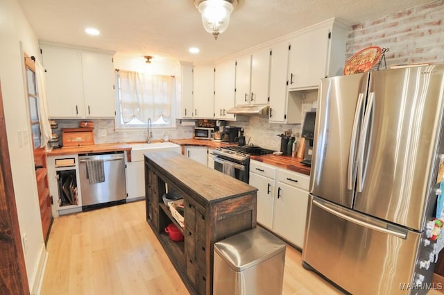 kitchen with butcher block counters, white cabinetry, stainless steel appliances, and a sink