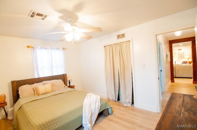 bedroom featuring baseboards, visible vents, ceiling fan, and light wood finished floors