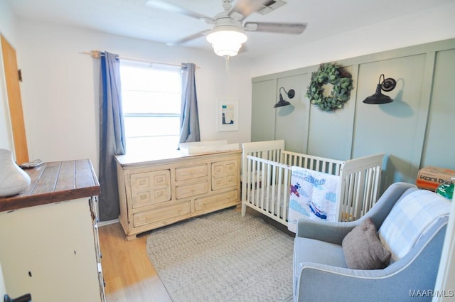 bedroom featuring light wood-type flooring, a nursery area, visible vents, and a ceiling fan