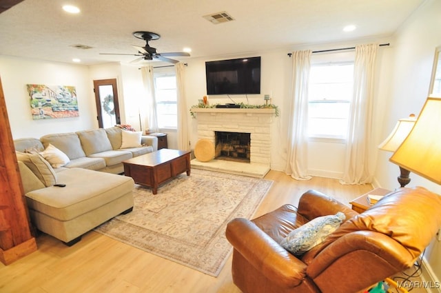 living room with a stone fireplace, light wood-type flooring, visible vents, and recessed lighting