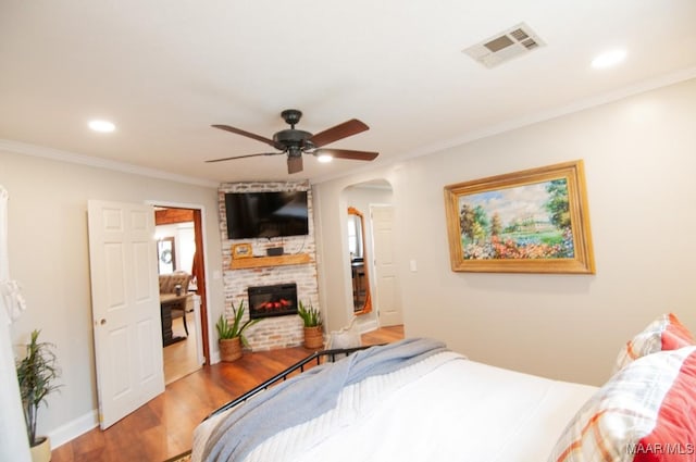 bedroom featuring visible vents, wood finished floors, crown molding, a brick fireplace, and recessed lighting