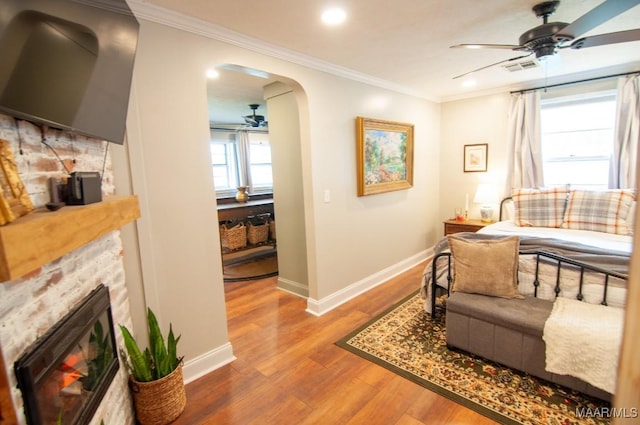 living room featuring arched walkways, ornamental molding, a glass covered fireplace, ceiling fan, and wood finished floors