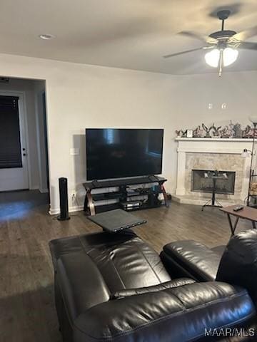 living area with dark wood-style floors, a fireplace with raised hearth, and a ceiling fan