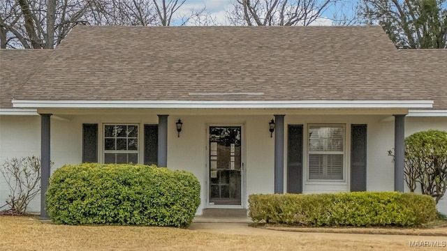 entrance to property with stucco siding, a porch, and roof with shingles