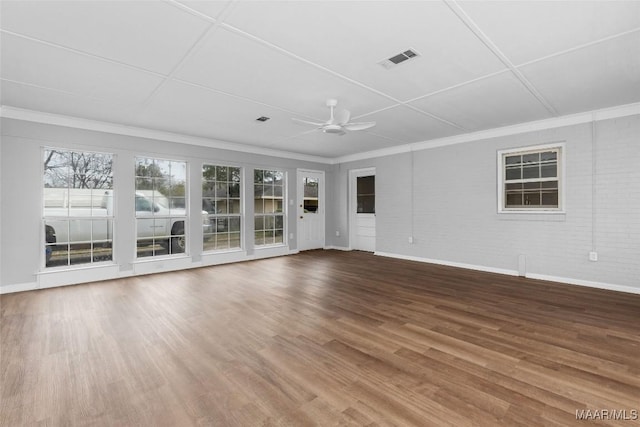 unfurnished living room with visible vents, brick wall, ceiling fan, ornamental molding, and wood finished floors