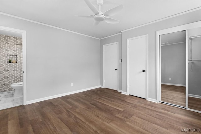 unfurnished bedroom with ornamental molding, connected bathroom, ceiling fan, wood finished floors, and baseboards