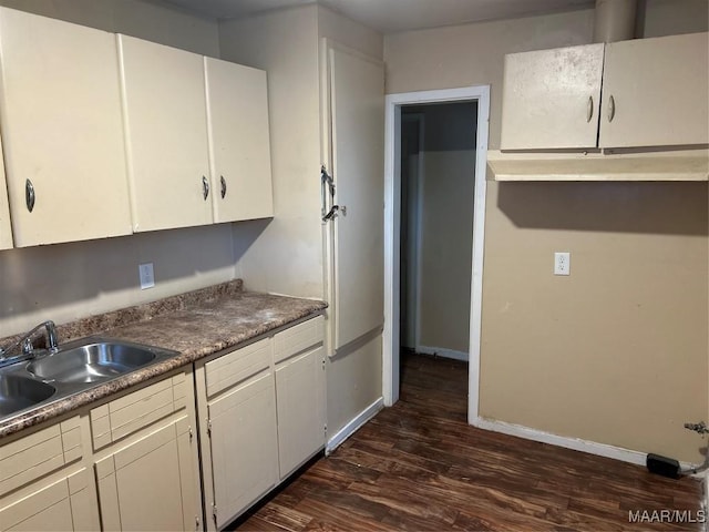 kitchen with baseboards, dark countertops, dark wood-type flooring, white cabinetry, and a sink