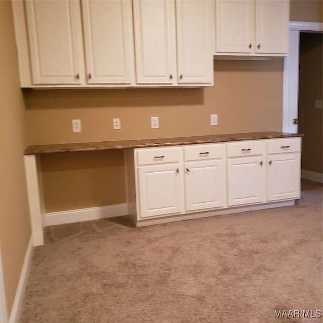 kitchen featuring baseboards, light colored carpet, dark countertops, built in study area, and white cabinetry