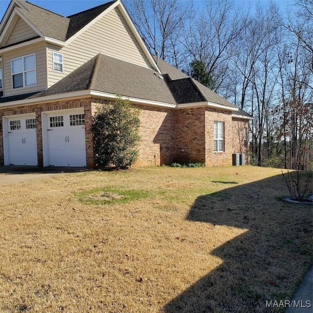 view of side of property featuring a garage, brick siding, a shingled roof, a yard, and driveway