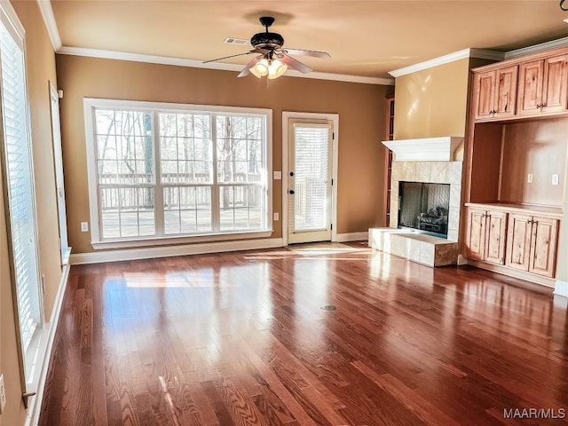 unfurnished living room featuring baseboards, wood finished floors, a tile fireplace, and crown molding