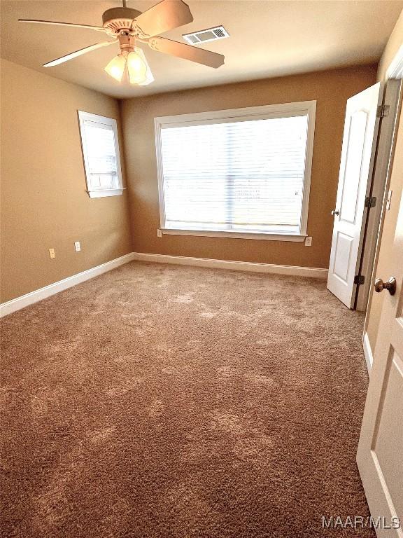 spare room with carpet floors, a ceiling fan, visible vents, and baseboards