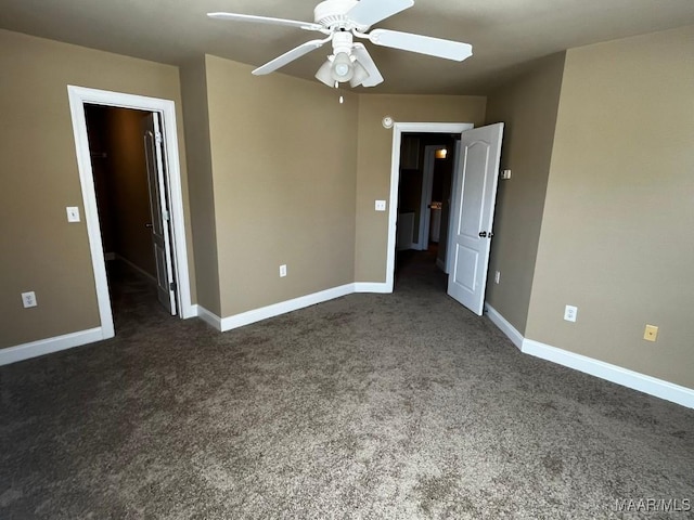 unfurnished bedroom featuring a spacious closet, baseboards, dark colored carpet, and a ceiling fan