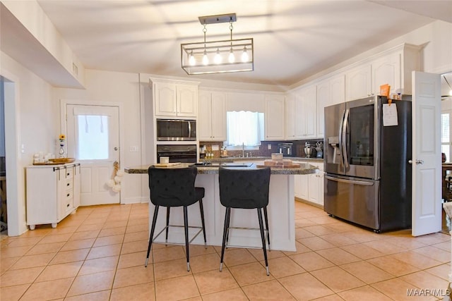 kitchen featuring light tile patterned floors, stainless steel appliances, white cabinets, a center island, and tasteful backsplash