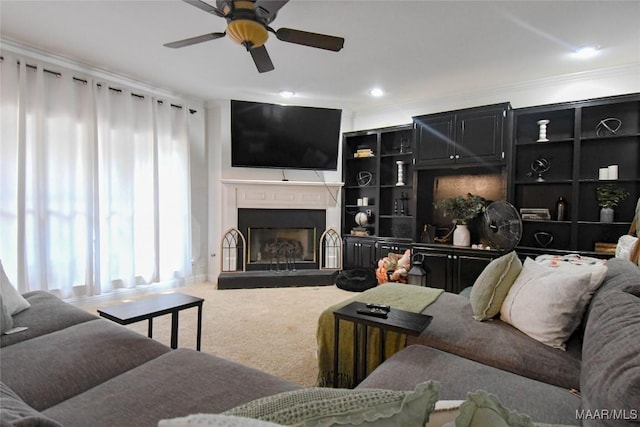 living area with a fireplace with raised hearth, ornamental molding, carpet flooring, and a ceiling fan