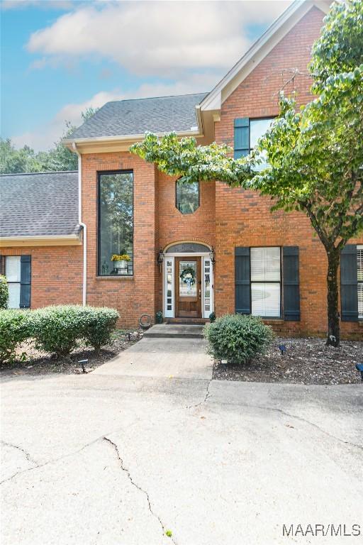 entrance to property featuring brick siding and a shingled roof