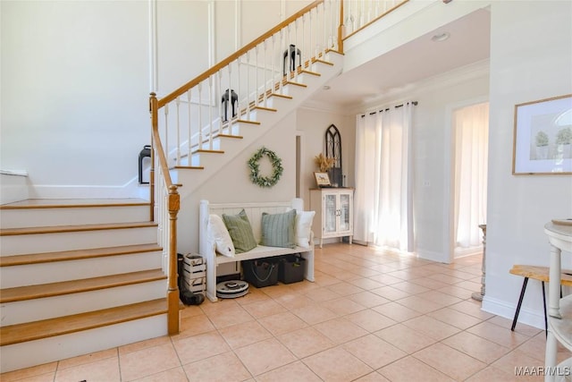 stairway featuring crown molding, a towering ceiling, baseboards, and tile patterned floors