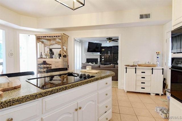 kitchen with a fireplace, light tile patterned floors, white cabinetry, dark stone counters, and black appliances