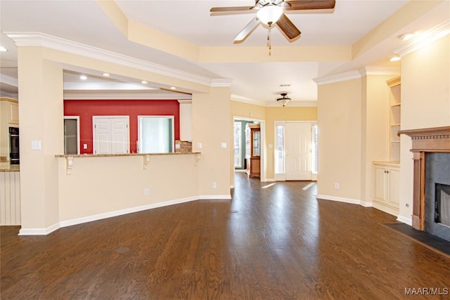 unfurnished living room with dark wood-style flooring, a raised ceiling, baseboards, and a tiled fireplace