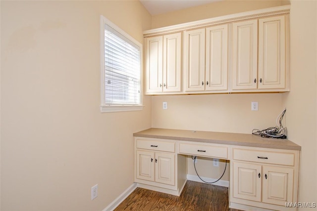 unfurnished office with dark wood-style floors, built in desk, and baseboards