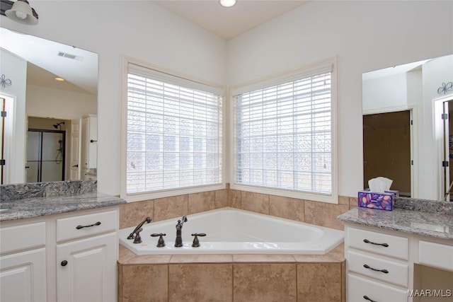 bathroom featuring a garden tub, a shower stall, visible vents, and two vanities