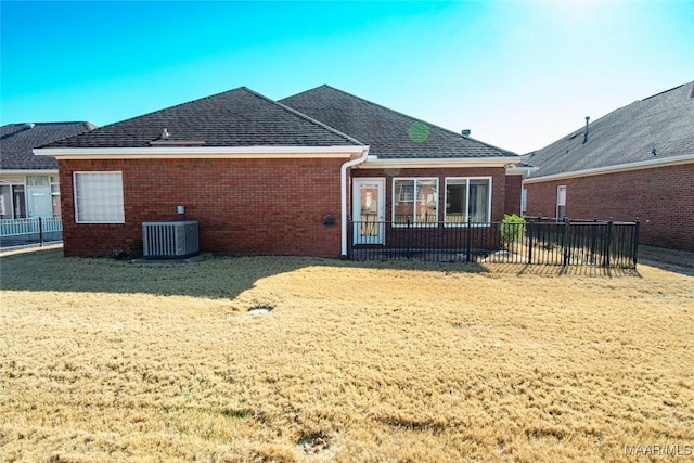 rear view of house featuring central air condition unit, brick siding, a shingled roof, fence, and a lawn